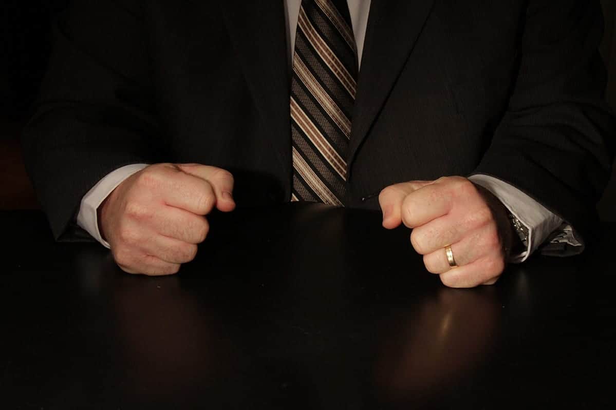 Mains serrées en poings sur une table noire, homme en veste noire et cravate à rayures