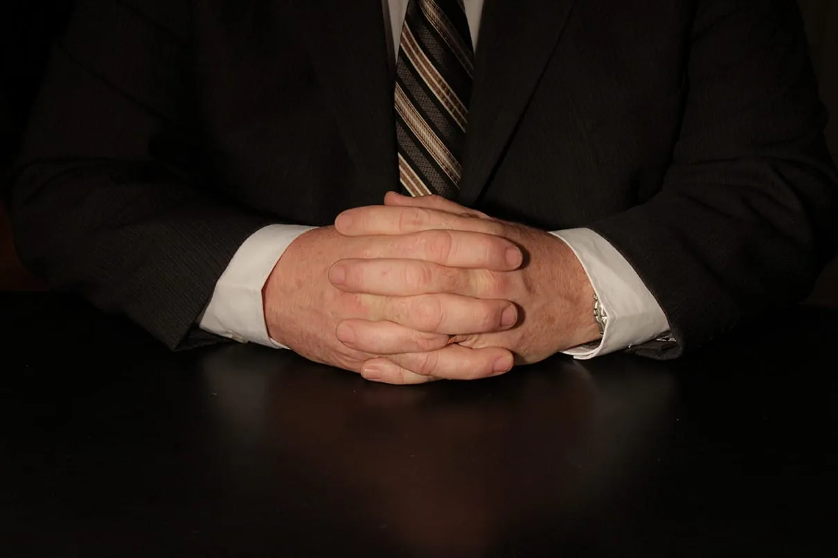The Importance of Hands in Communication (Part One) 1 Crossed hands of a man in a suit jacket with a white shirt and a striped tie on a black table
