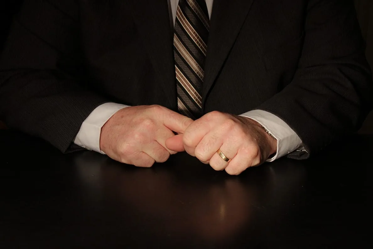 The Importance of Hands in Communication (Part One) 2 Hands of a man in a suit clasping his fingers on a black table